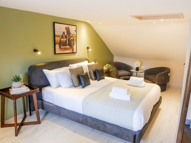 Bright attic bedroom with double bed, green accent wall, armchair and framed wall art