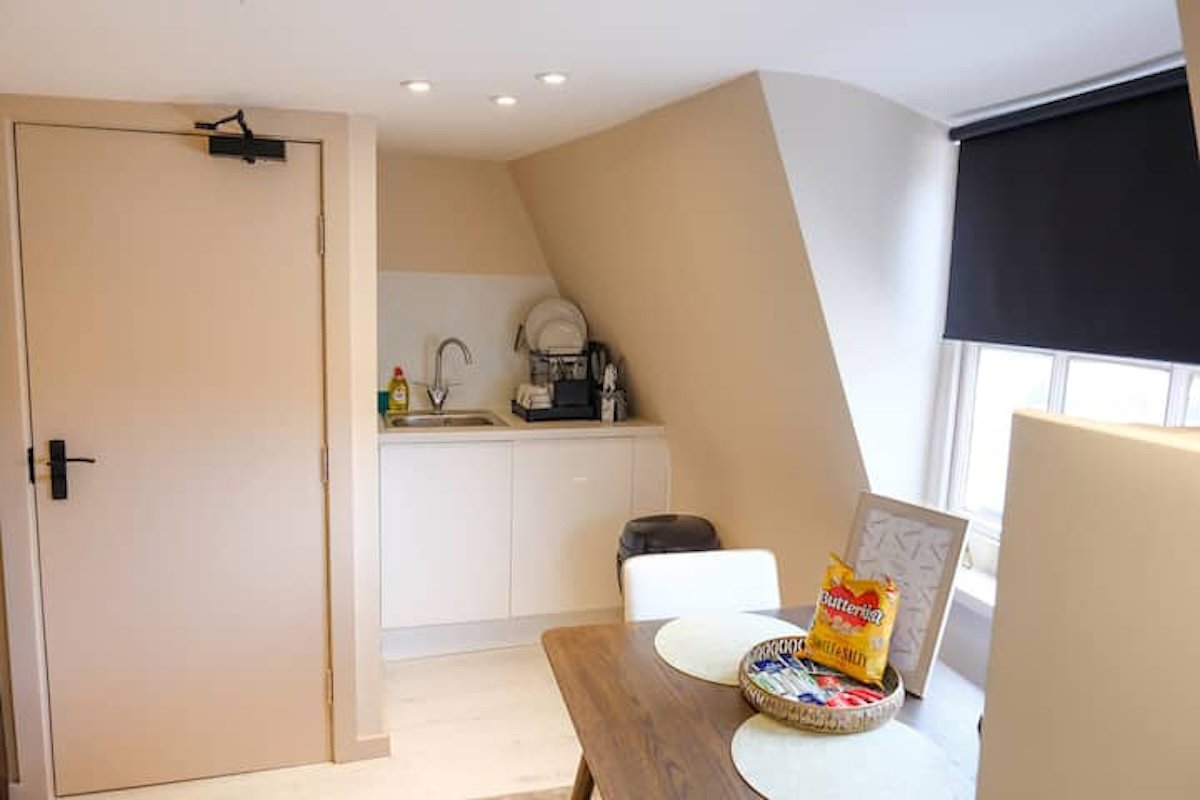 Compact attic room with sloped ceiling, wooden desk, white storage cabinet and kettle