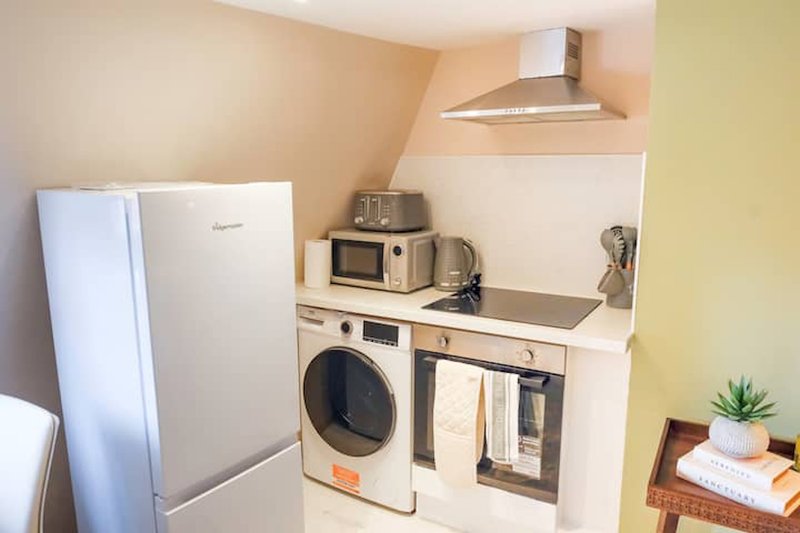 Compact kitchen with white appliances, washing machine, microwave and range hood