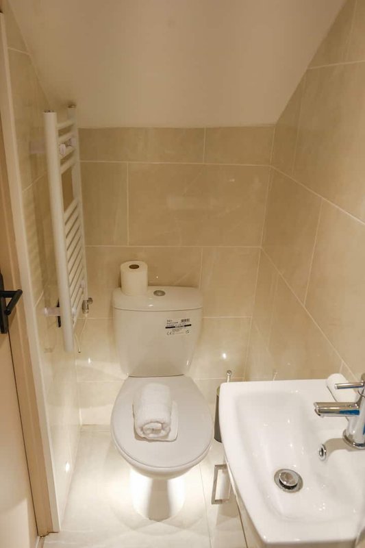 Small bathroom with toilet, sink, towel rail and cream tile walls
