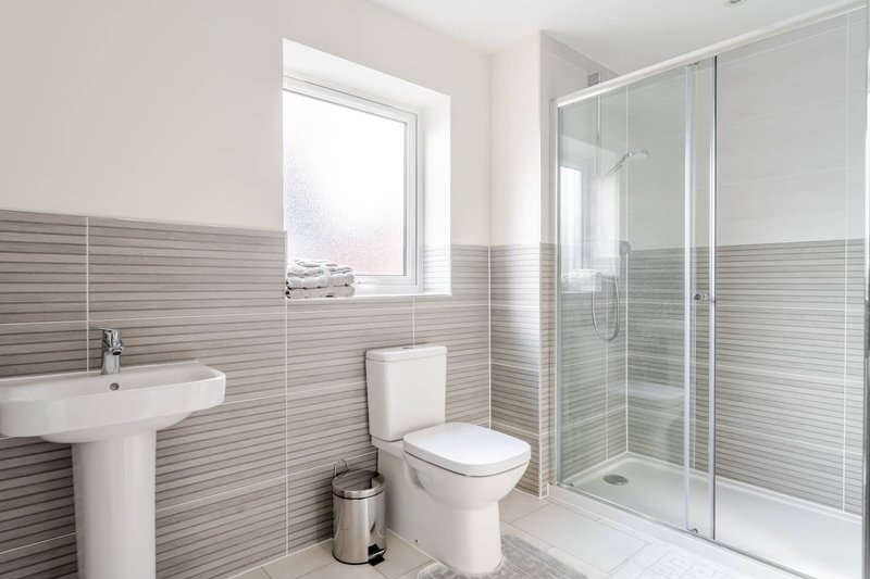 Modern bathroom with striped tile walls, pedestal sink, toilet, and glass shower enclosure