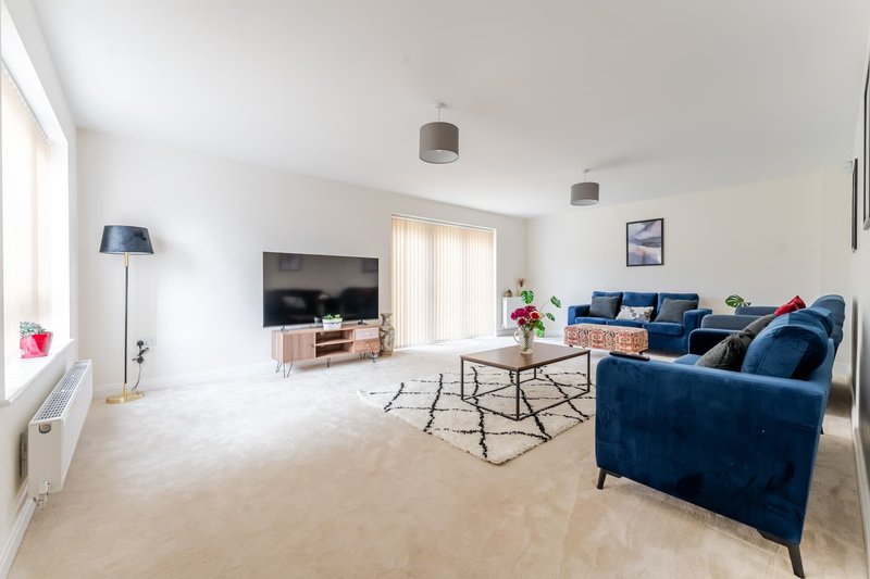 Spacious living room with blue velvet sofa, TV unit, wooden floor and pendant lighting