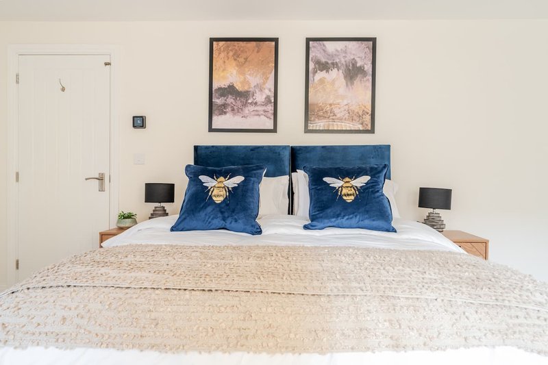 Modern bedroom with blue velvet headboard, white bedding, framed artwork above bed, and bedside tables
