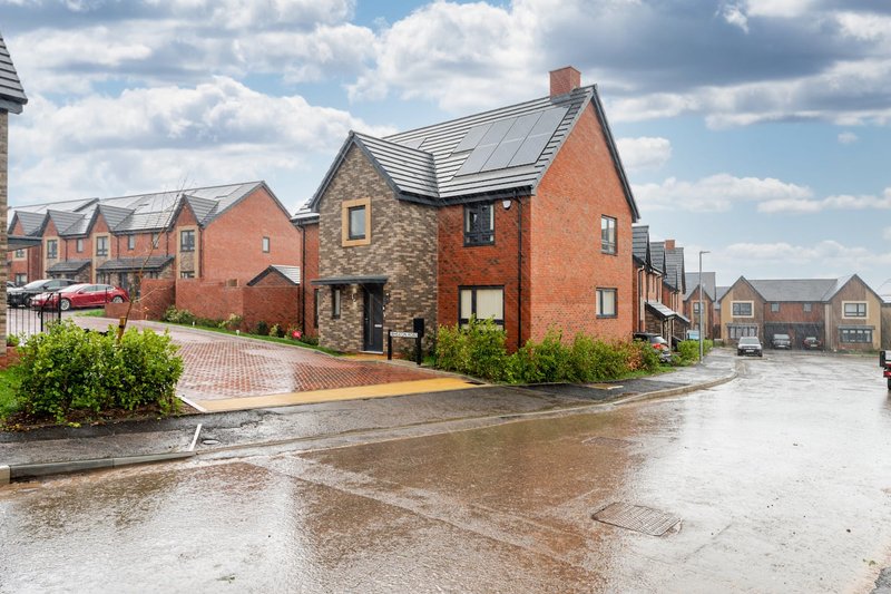 Red brick detached house with slate roof, stone accents, driveway and front landscaping