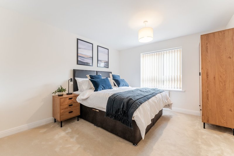 Bright bedroom with double bed, blue bedding, wooden nightstand and wardrobe