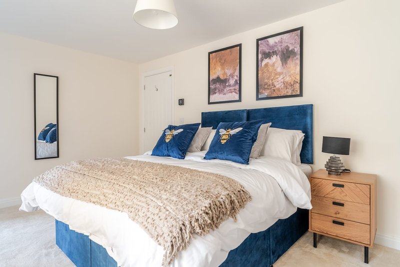 Bedroom with blue upholstered bed, beige bedding, wooden nightstand, framed wall art, and mirror