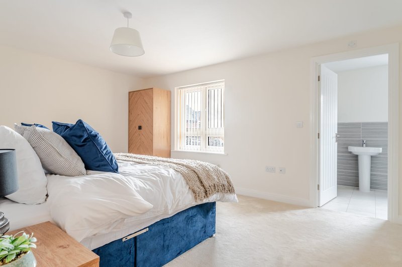 Bright modern bedroom with double bed, blue velvet headboard, and ensuite bathroom visible through open door