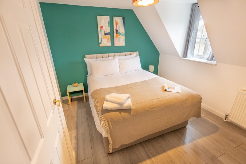 Bright attic bedroom with double bed, teal accent wall, wooden floor and sloped ceiling