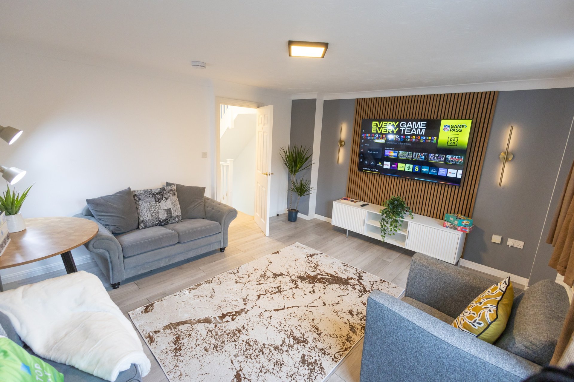 Modern living room with grey sofas, neutral rug, wall-mounted TV and plants