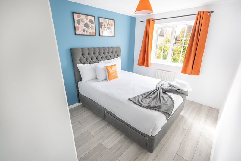 Bright bedroom with double bed, grey upholstered headboard, blue accent wall, orange curtains