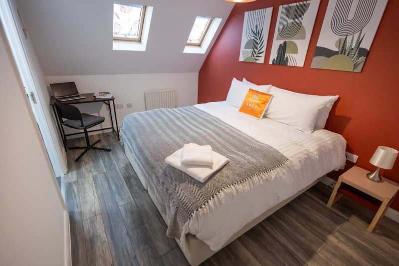 Bright bedroom with double bed, orange accent wall, skylights and wooden flooring