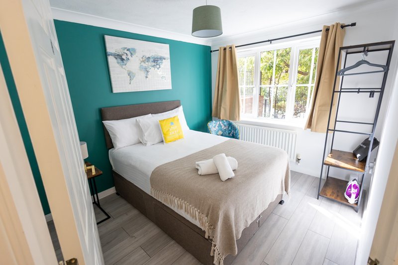Bright bedroom with teal accent wall, double bed, yellow cushion, and large window with garden views