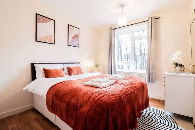 Bright bedroom with double bed, orange bedding, white furniture and framed wall art