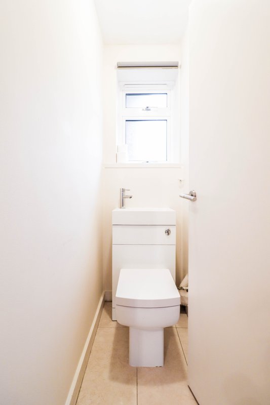 Compact bathroom with white toilet, small sink vanity and window above