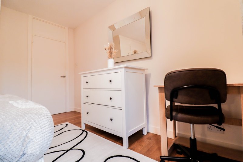 Bright bedroom with white dresser, black chair, mirror, and wooden flooring