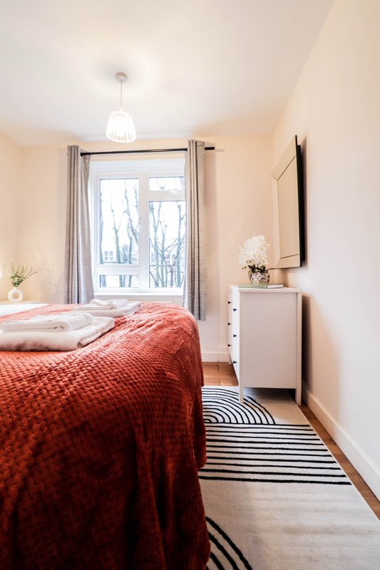 Bright bedroom with double bed, red bedspread, white nightstand and pendant light