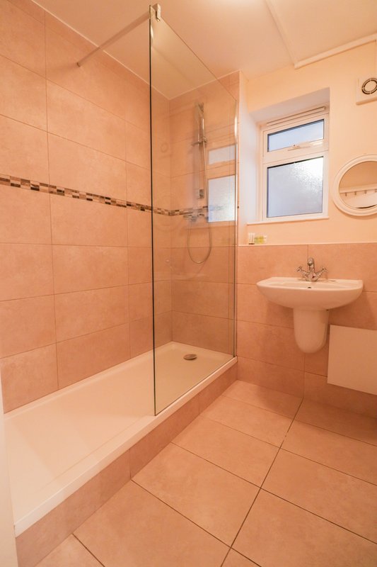 Modern bathroom with walk-in shower, pedestal sink, and terracotta tile throughout