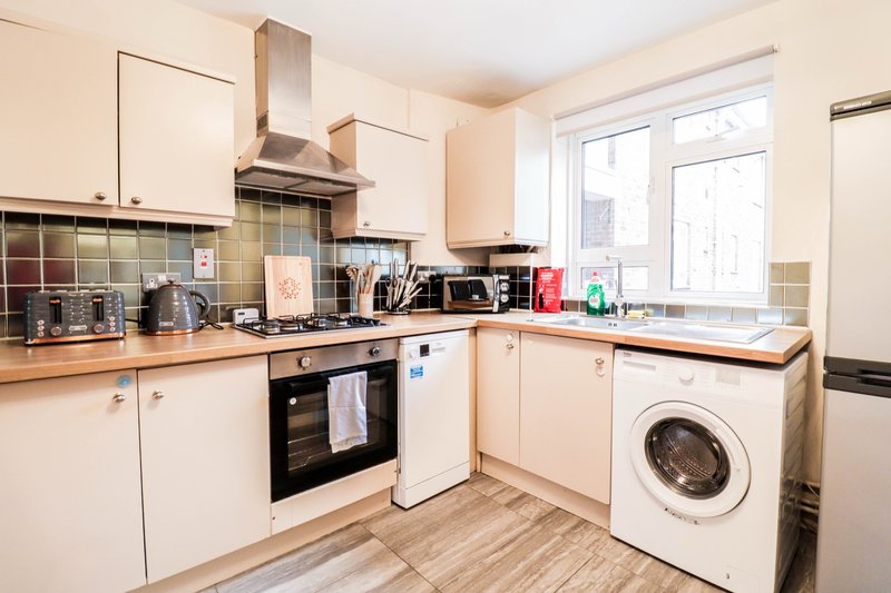 Modern kitchen with white cabinetry, stainless steel cooker hood, washing machine, and wood-effect flooring