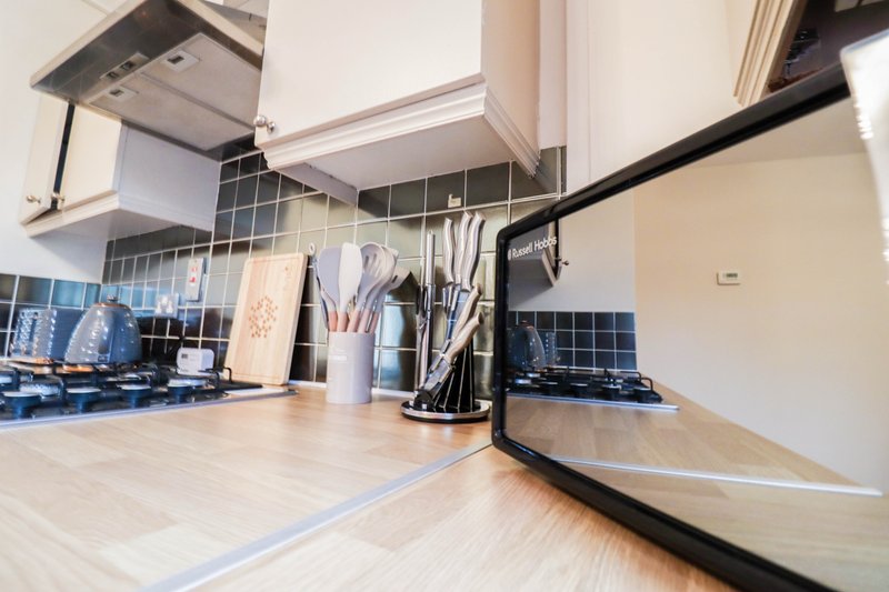 Modern kitchen with white cabinetry, dark tile backsplash, wooden countertop, and stainless steel appliances