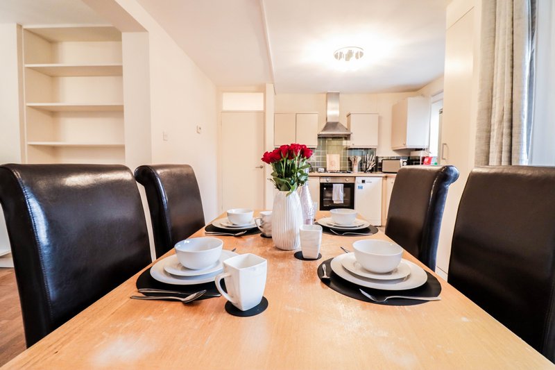 Open-plan dining and kitchen area with wooden table, black leather chairs and place settings