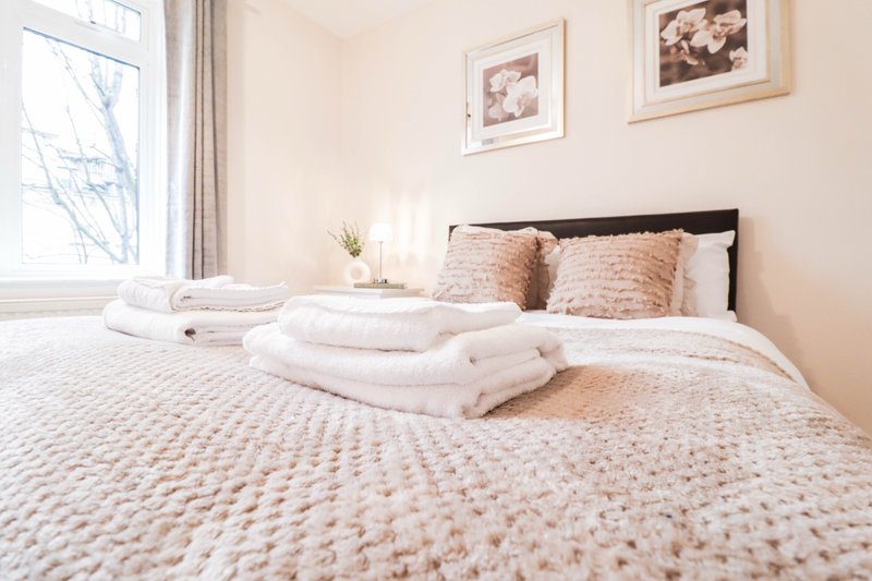 Bright bedroom with neatly made bed, stacked towels, and framed wall art
