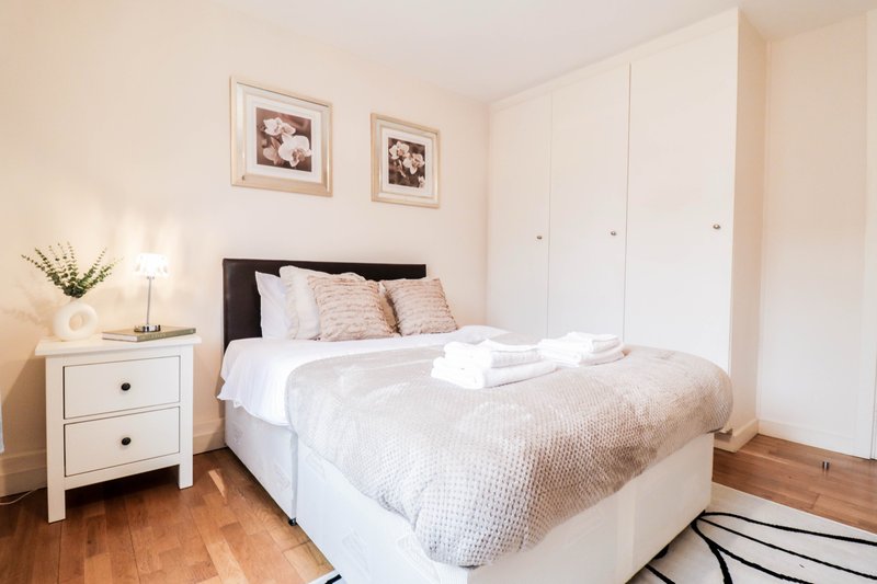 Bright bedroom with double bed, white bedside table, wooden floor and wardrobe
