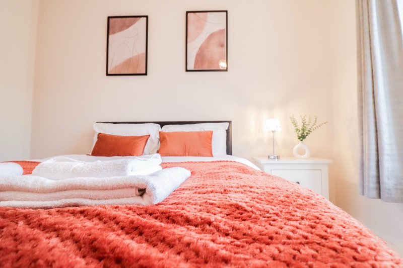 Bright bedroom with double bed, coral bedding, framed wall art, and white bedside table