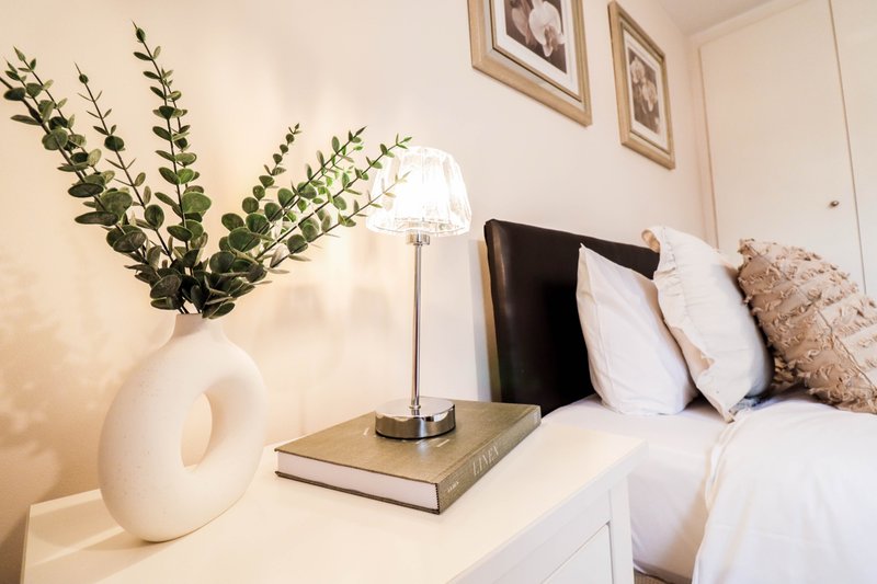 Bedroom nightstand with white vase, greenery, table lamp, and stacked books
