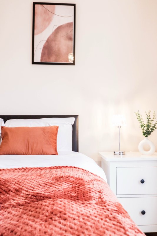 Bedroom with single bed, orange bedding, white nightstand and framed abstract wall art