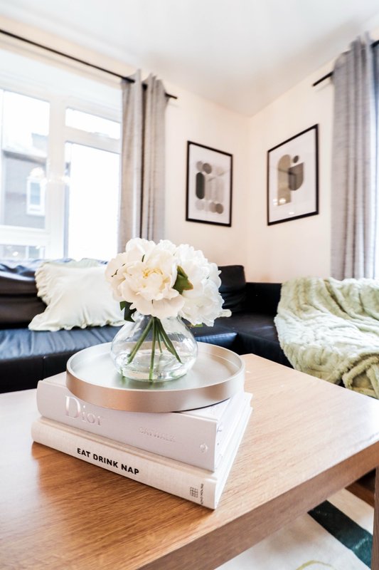 Modern living room with black sofa, wooden coffee table, fresh flowers in vase, and large windows with curtains