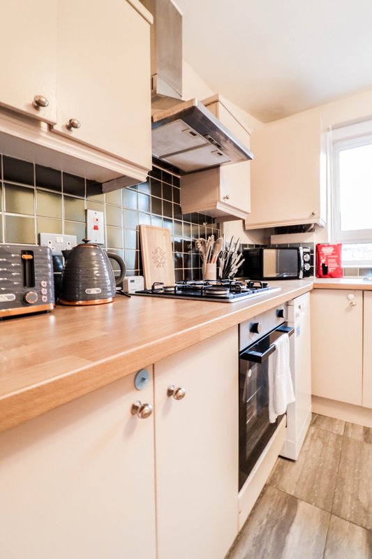 Modern kitchen with white cabinetry, wooden countertop, gas hob and range hood