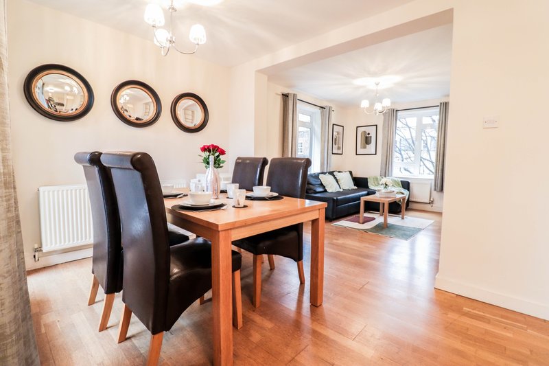 Open-plan dining and living area with wooden table, black chairs, wall clocks, and hardwood flooring