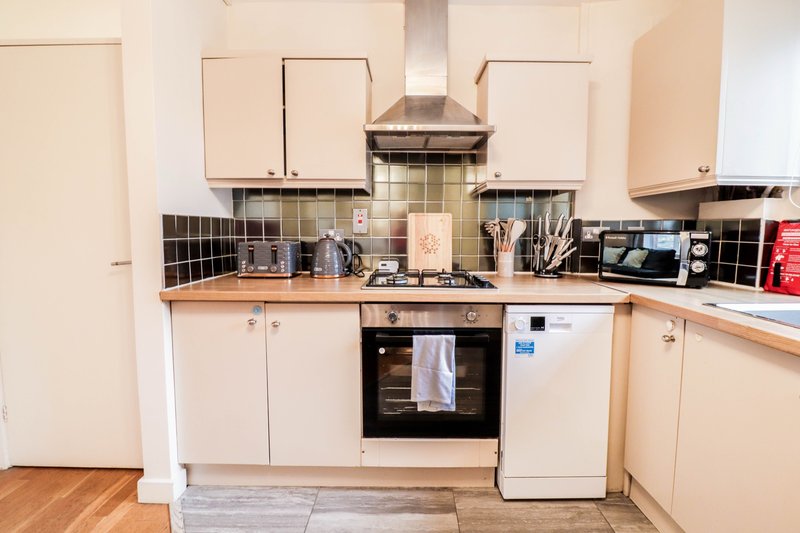 Kitchen with cream cabinets, black tile backsplash, gas range hood and integrated appliances