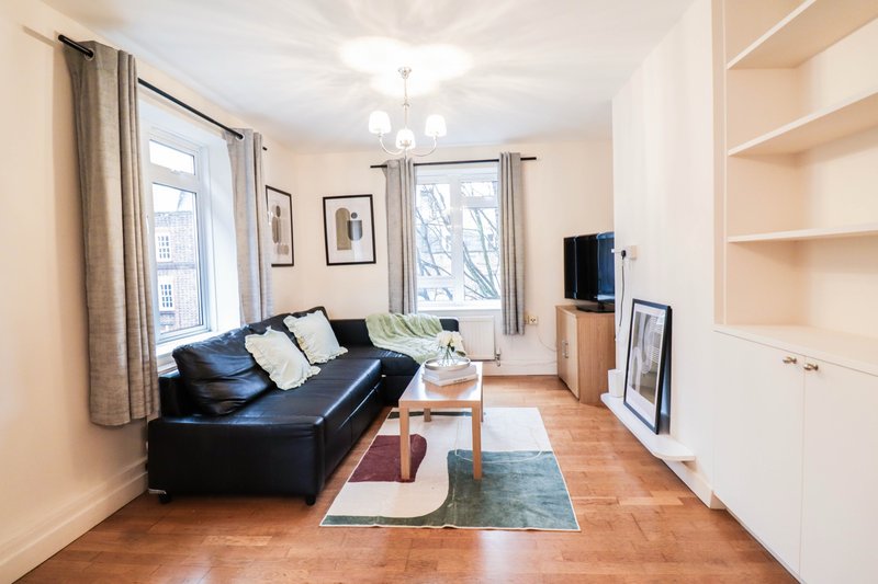 Bright living room with black leather sofa, wooden floor, TV, and cream shelving