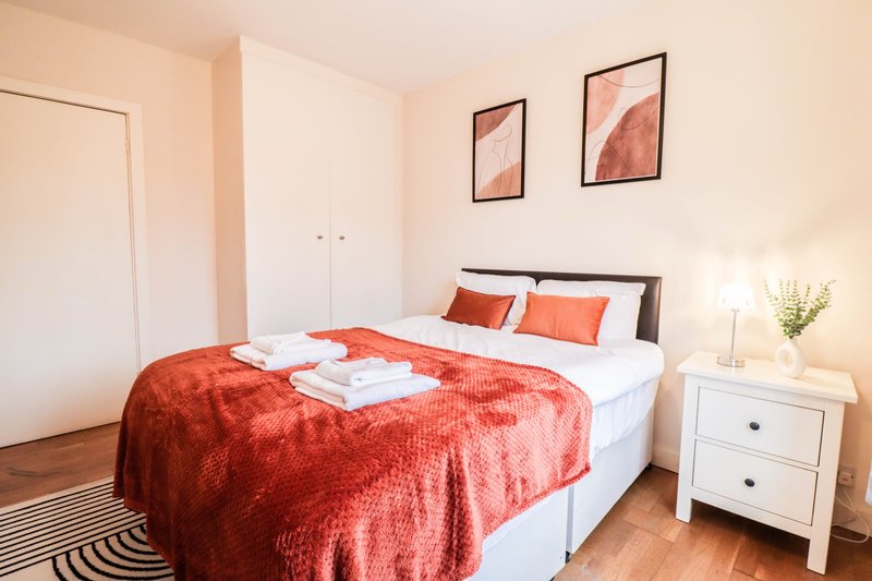 Bright bedroom with double bed, red throw blanket, white pillows, bedside table and framed wall art