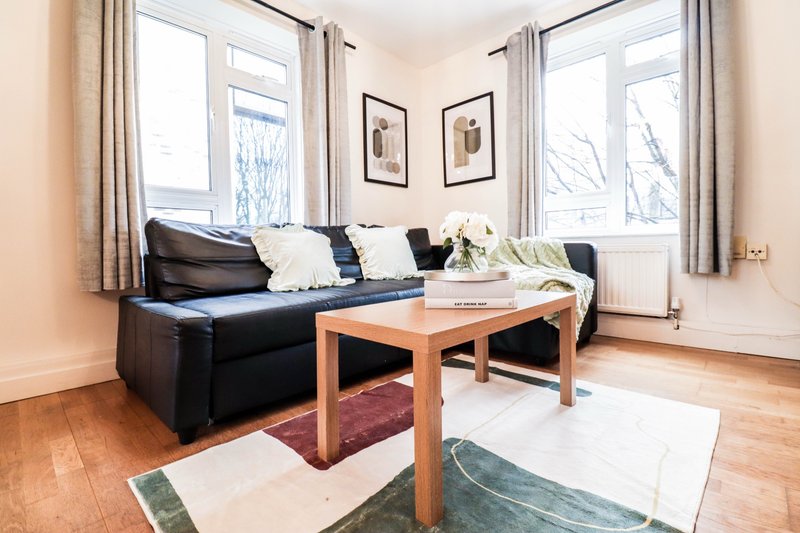 Bright living room with black leather sofa, wooden coffee table, framed wall art and large windows