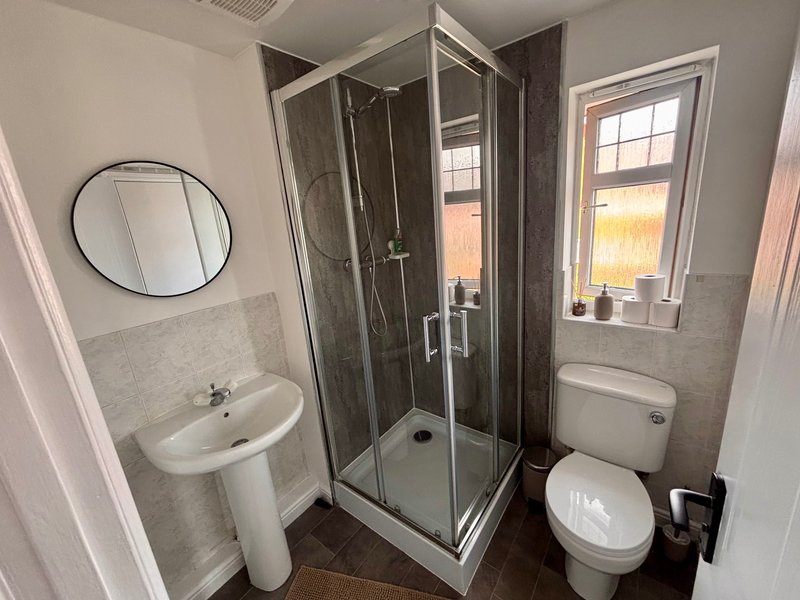Modern bathroom with shower enclosure, pedestal sink, toilet and round mirror