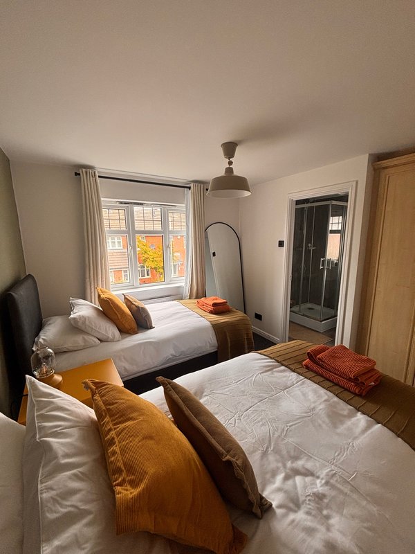 Bright bedroom with two single beds, mustard yellow bedding, window with autumn view, and door to ensuite