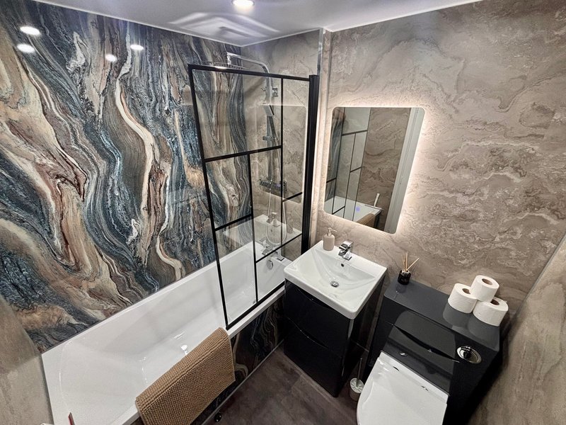 Modern bathroom with bathtub, glass shower enclosure, black vanity and illuminated mirror