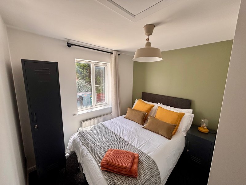 Modern bedroom with double bed, orange cushions, green accent wall and pendant light