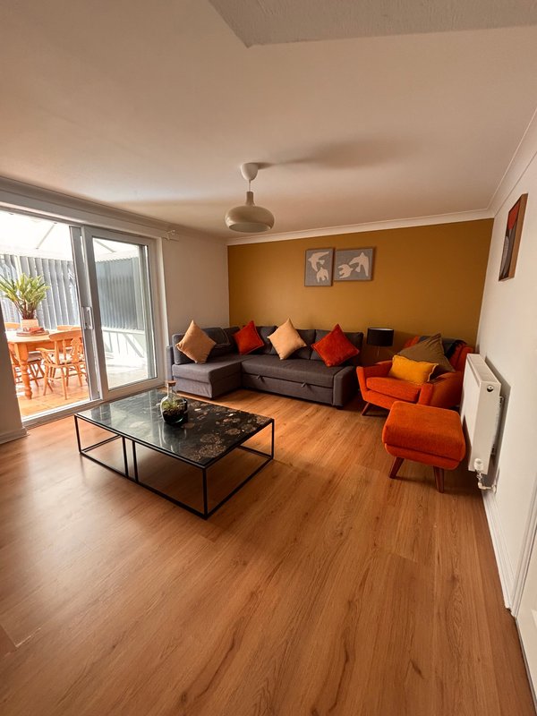 Living room with orange accent wall, dark sofa, colorful cushions, wooden floor and glass doors to patio