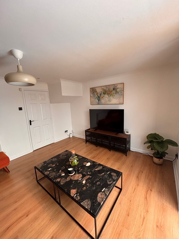 Living room with wooden flooring, TV on stand, black patterned coffee table, and white door