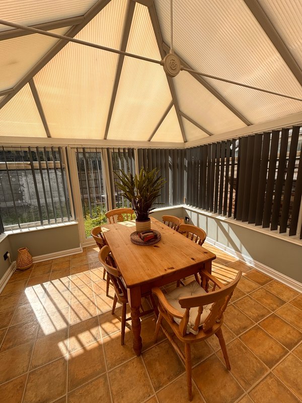 Conservatory with wooden dining table, chairs, potted plant and glass roof panels