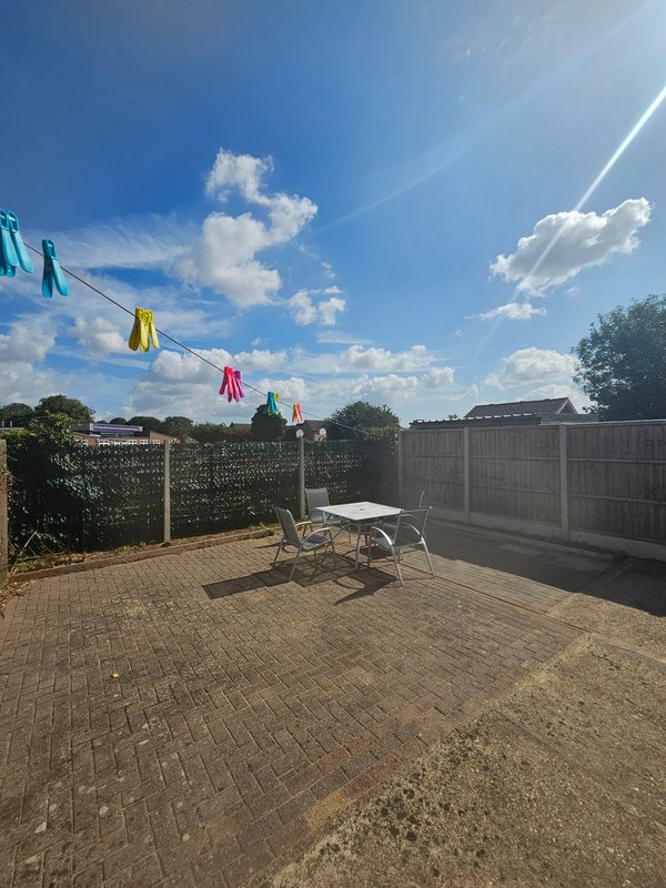 Patio garden with clothesline, deck chair, and wooden fence under blue sky