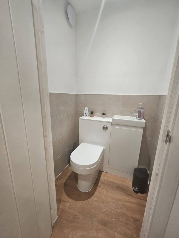 Small bathroom with white toilet, sink vanity, wooden floor and tiled walls