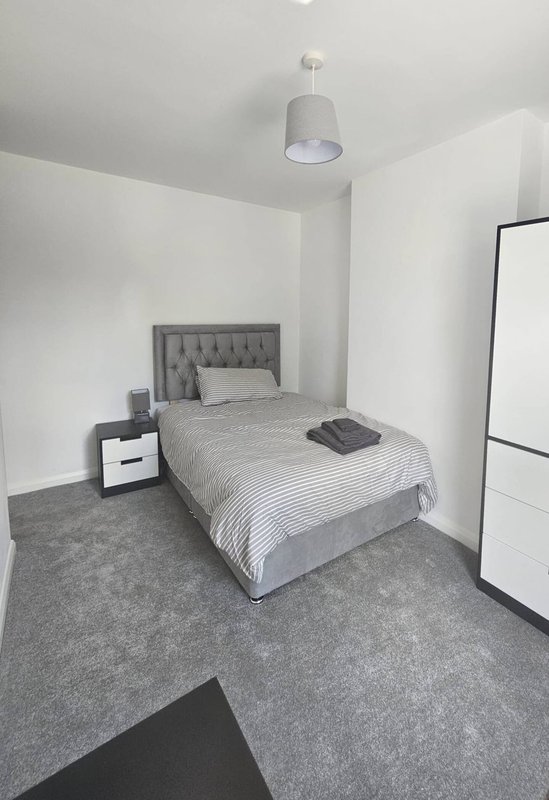 Minimalist bedroom with single bed, gray headboard, white nightstand, and pendant light