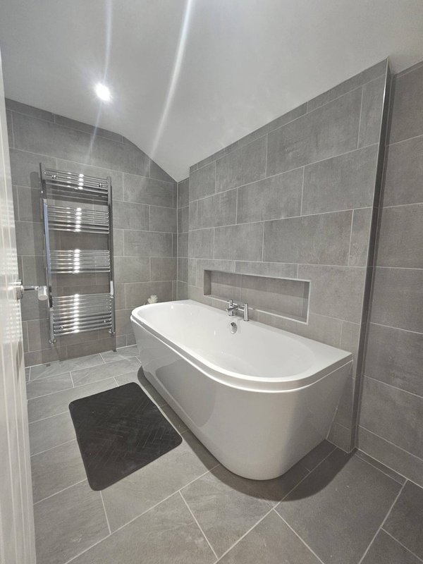 Modern bathroom with freestanding white bathtub, gray tile walls, and heated towel rail