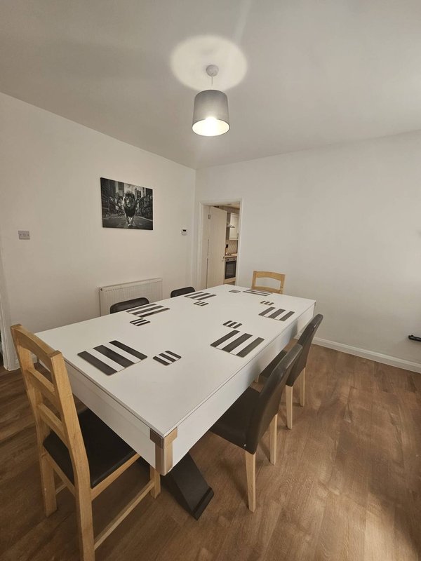 Dining room with white table, wooden chairs, ceiling light, and framed wall art.
