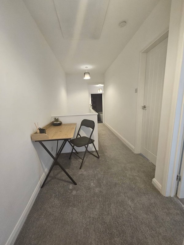 Narrow hallway with desk, folding chair, overhead lighting and white doors