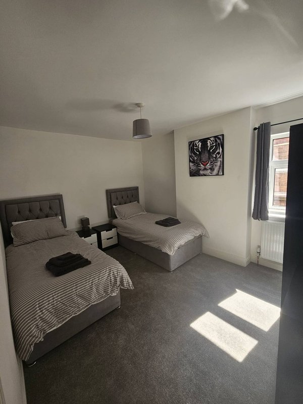 Twin bedroom with two single beds, dark headboards, bedside table, and window with curtains